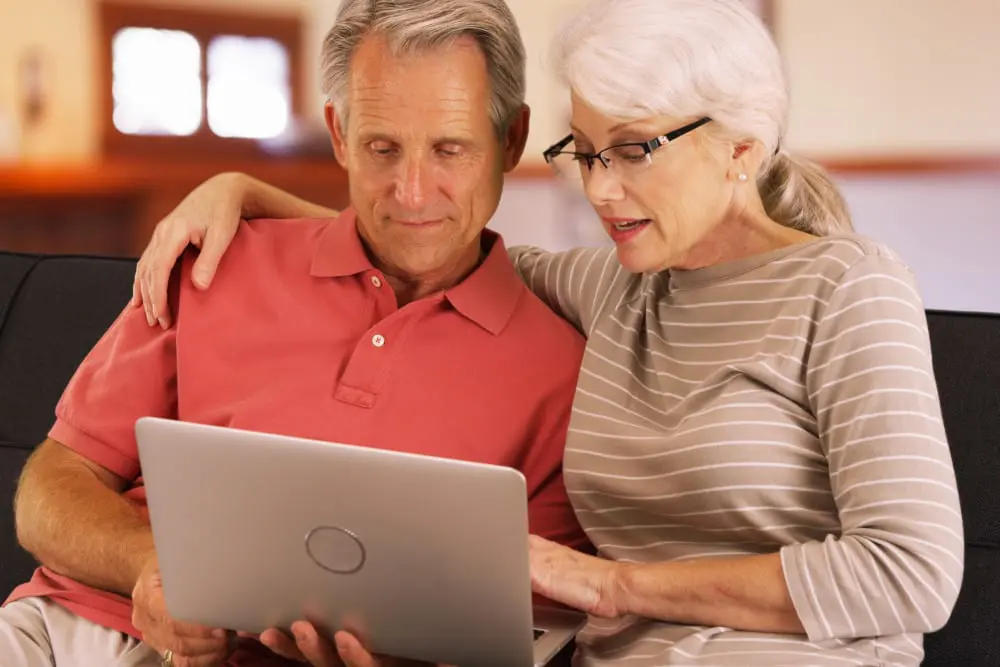 Mature couple sitting on a couch looking at a laptop.