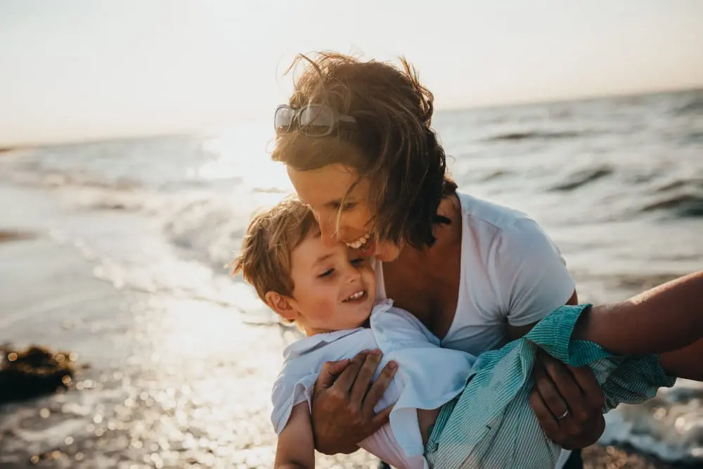 Mother holding and playing with son along the beach.